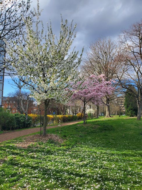 An expansive, lush hillside garden scene showcasing a variety of trees with different shades of green, some with fresh spring leaves and others with darker foliage, creating a layered landscape. The h